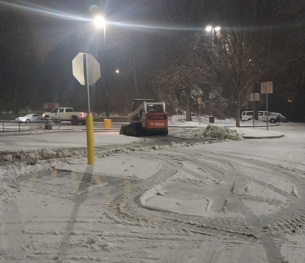 Bobcat skid steer clearing snow from a Greensboro parking lot at night