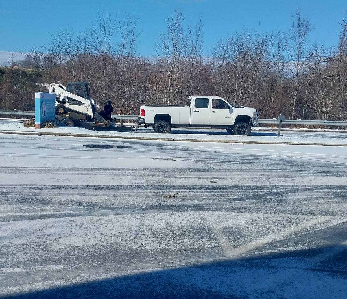 Green Limb truck and skid steer on a trailer at a snow-covered Greensboro lot